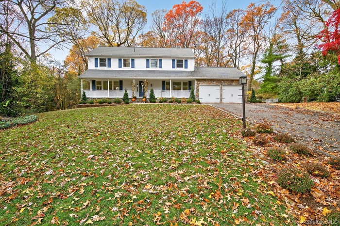 View of front facade featuring a porch, an attached garage, driveway, a front lawn, and roof with shingles