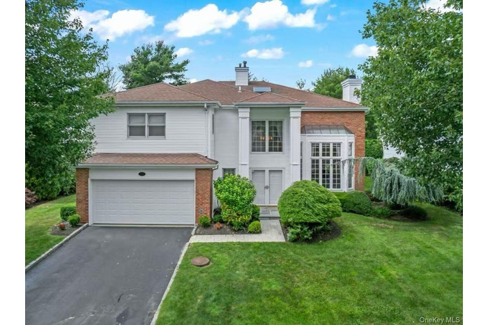 View of front of property featuring a chimney, driveway, brick siding, a garage, and a front lawn