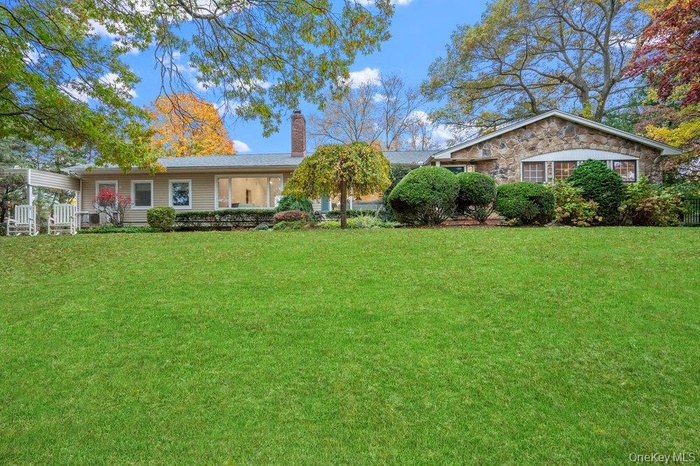 View of front facade featuring a front yard, a chimney, and stone siding