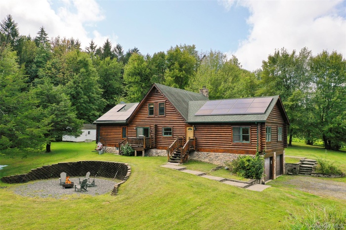 Rear view of house with a fire pit, solar panels, a chimney, and a garage