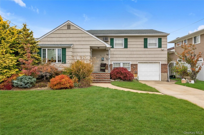 View of front of property with a front yard, a garage, concrete driveway, brick siding, and a shingled roof