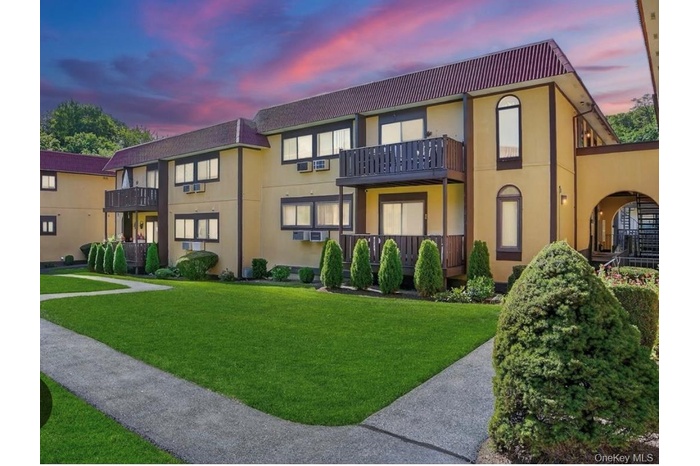 Back of house at dusk featuring stucco siding, a lawn, and a balcony