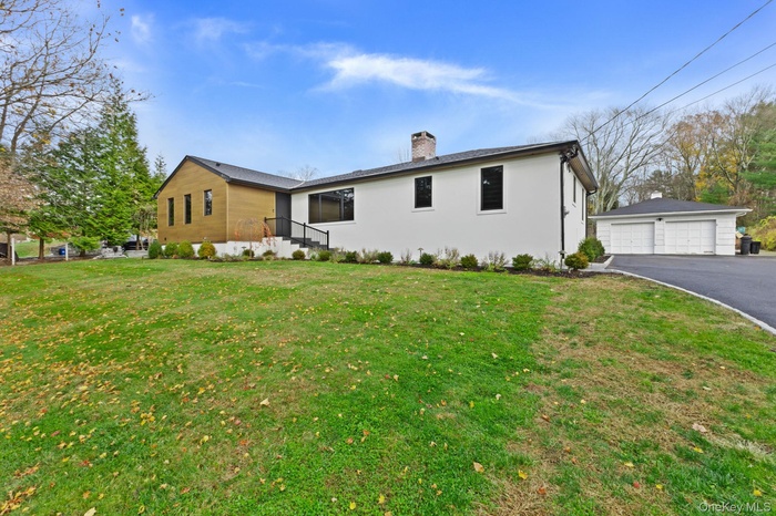 View of front of home with a detached garage, stucco siding, a chimney, an outbuilding, and a front lawn