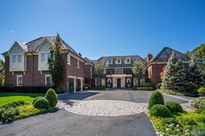 View of front of property with asphalt driveway, brick siding, a high end roof, and a chimney