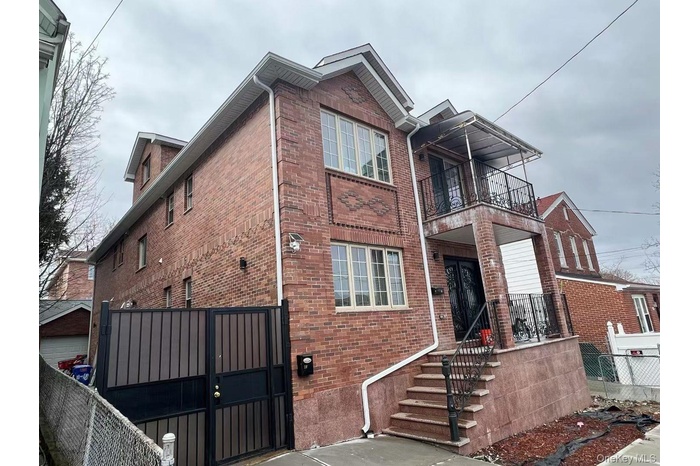 View of front of property featuring brick siding, a gate, and a balcony