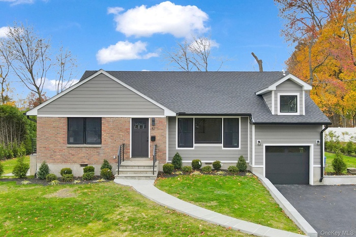 View of front facade with a front lawn, a shingled roof, a garage, asphalt driveway, and brick siding