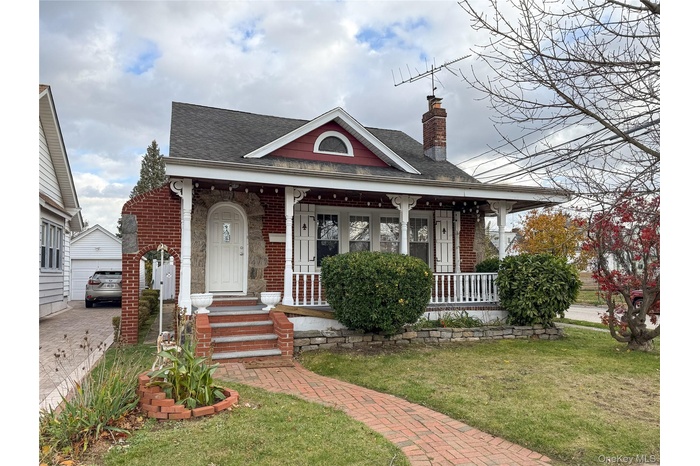 View of front facade featuring a front yard, a chimney, a shingled roof, and brick siding