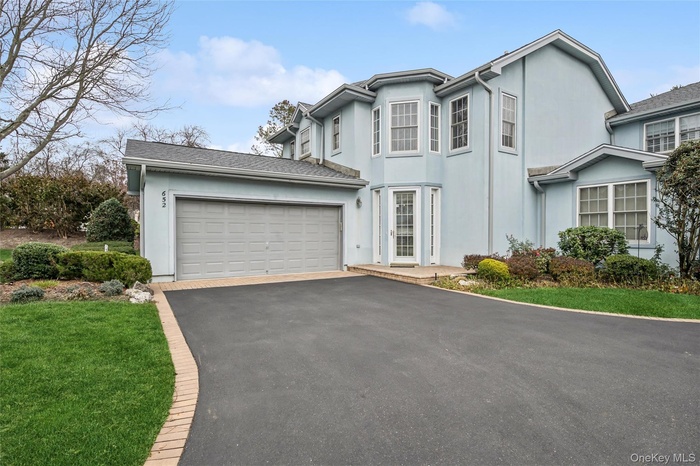 View of front of property featuring asphalt driveway, stucco siding, a garage, and a front yard