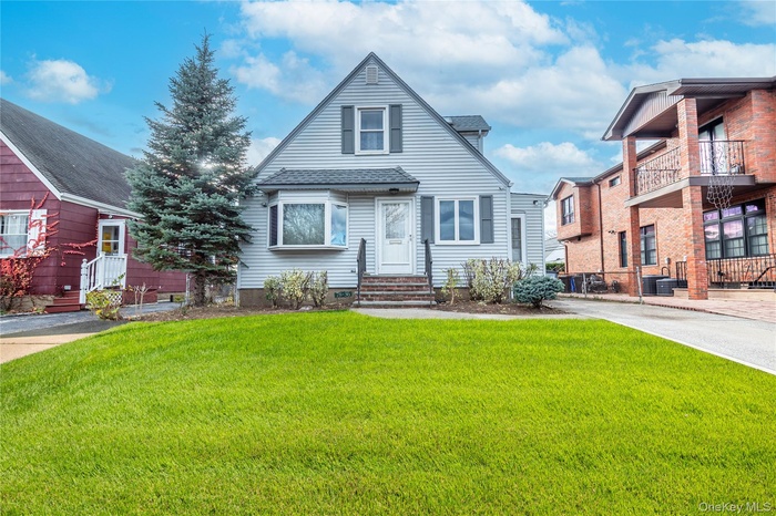 View of front of property featuring a front yard, a balcony, and roof with shingles
