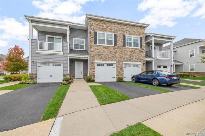 View of front facade with stone siding, a balcony, driveway, and a garage