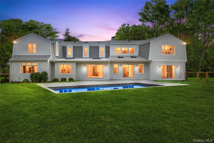 Back of property at dusk with a gambrel roof, a lawn, and a patio