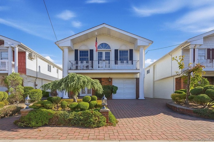 View of front of property with a balcony, decorative driveway, brick siding, and an attached garage