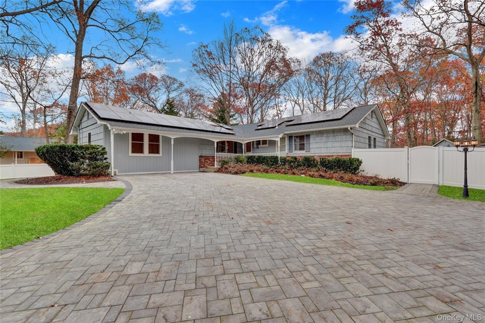 Single story home with decorative driveway, roof mounted solar panels, and a gate