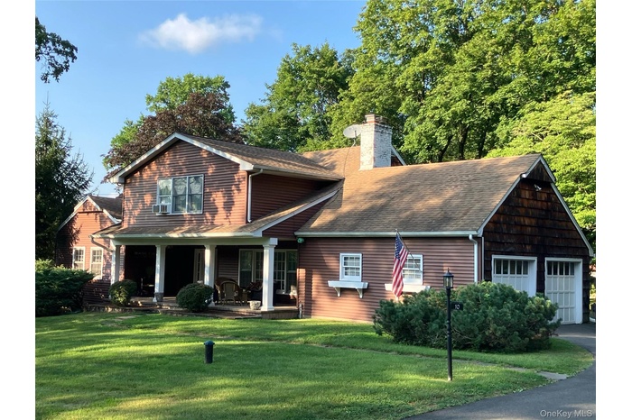 Back of property with a yard, roof with shingles, a chimney, covered porch, and driveway