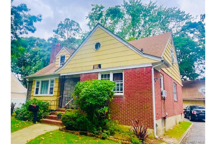 View of front of property featuring brick siding, a chimney, and a front lawn