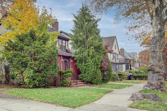 View of property hidden behind natural elements with a front yard, a chimney, and brick siding