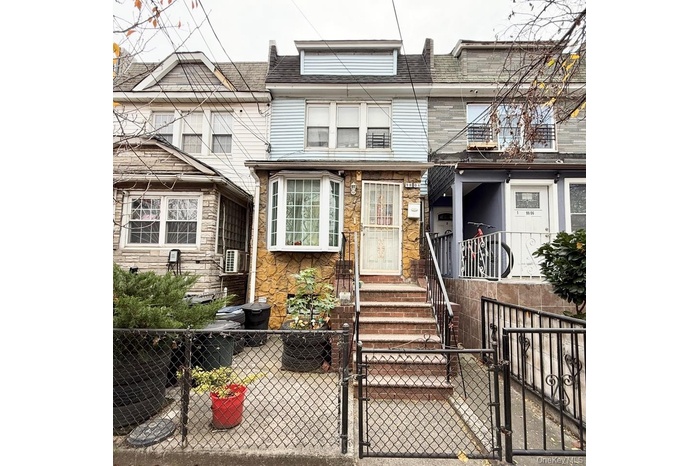 View of front of home featuring a gate, a fenced front yard, stone siding, and roof with shingles