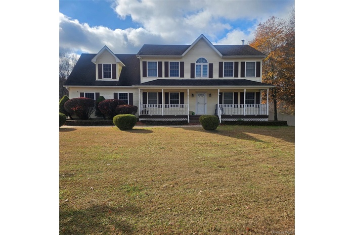 Colonial home featuring covered porch and a front yard