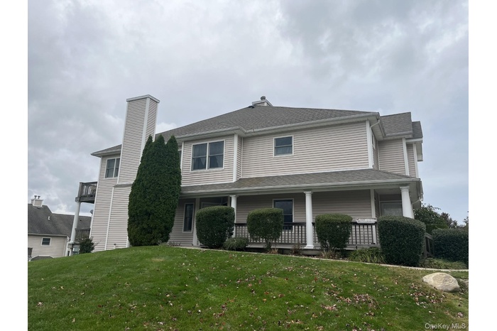 View of front of house with a front yard, roof with shingles, covered porch, and a chimney