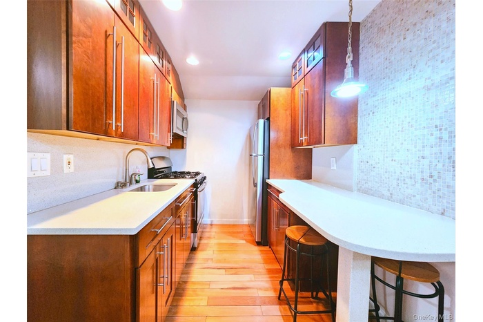 Kitchen featuring brown cabinetry, stainless steel appliances, tasteful backsplash, light wood-type flooring, and a kitchen breakfast bar