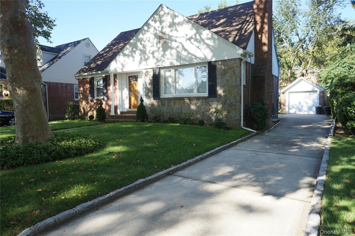 Tudor-style house with a front lawn, stone siding, an outdoor structure, a chimney, and a detached garage