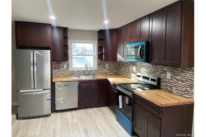 Kitchen with appliances with stainless steel finishes, dark brown cabinets, wooden counters, and recessed lighting
