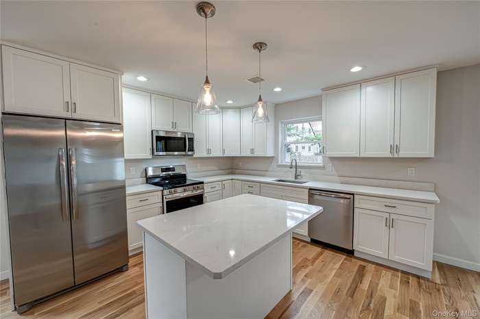 Kitchen with stainless steel appliances, white cabinets, decorative light fixtures, light stone countertops, and light wood-type flooring