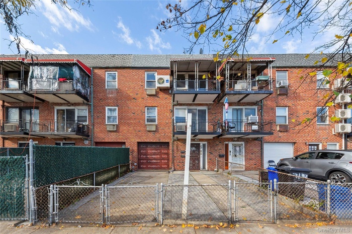 View of front of home with a gate, brick siding, driveway, and a balcony