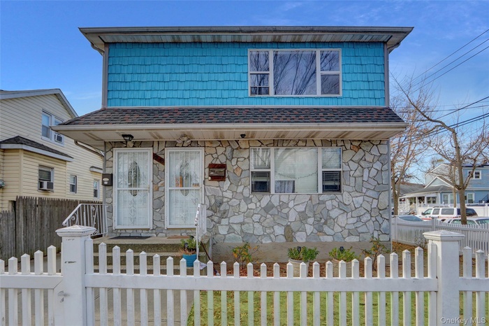 View of front of property featuring stone siding, a fenced front yard, and roof with shingles