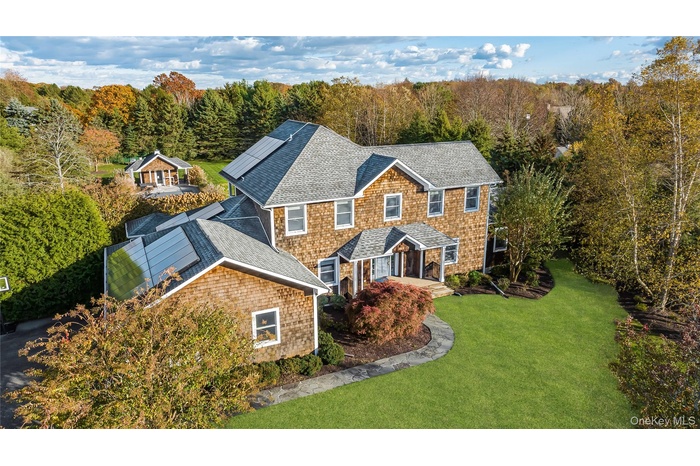 View of front facade with roof with shingles, a front yard, solar panels, and a forest view