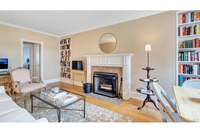 Living room with built in features, wood finished floors, baseboards, crown molding, and a fireplace with flush hearth
