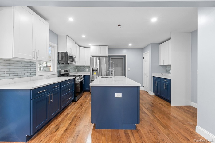 Kitchen with blue cabinetry, tasteful backsplash, white cabinetry, appliances with stainless steel finishes, and light wood-type flooring