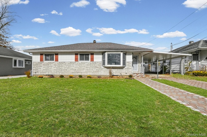 View of front facade with roof with shingles, an attached carport, a front yard, and stone siding