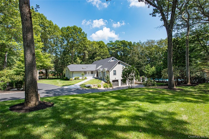 View of front of home with a front lawn, view of wooded area, a garage, and asphalt driveway
