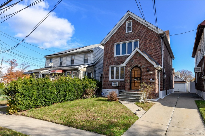 View of front of property featuring brick siding, an outbuilding, a front lawn, and a detached garage