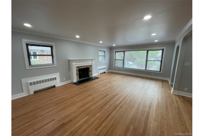 Unfurnished living room with crown molding, radiator heating unit, arched walkways, recessed lighting, and light wood finished floors