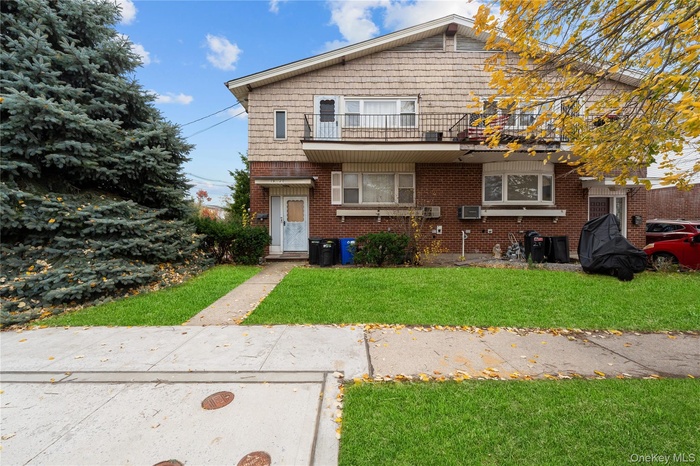 View of front of house with a front yard, brick siding, and a balcony