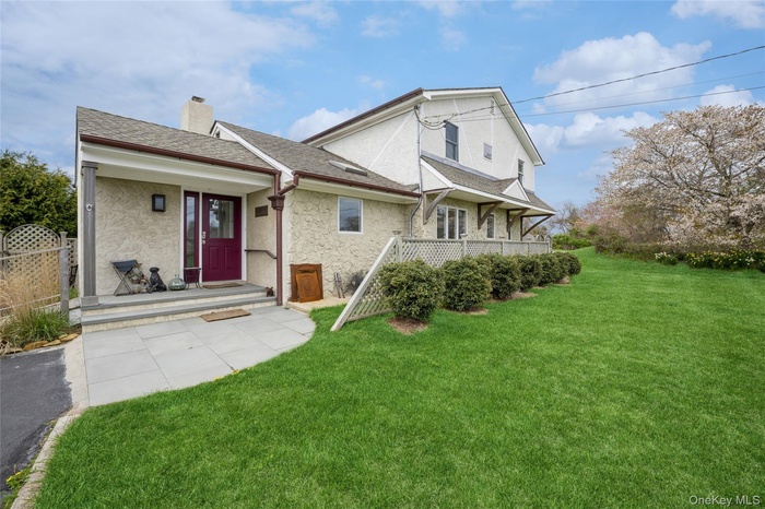 View of front of house with roof with shingles, stucco siding, a chimney, and a front yard