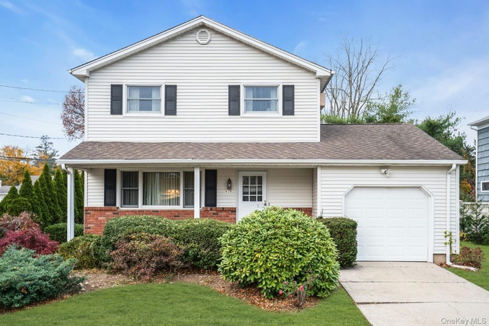 Traditional home featuring brick siding, an attached garage, a porch, a shingled roof, and driveway