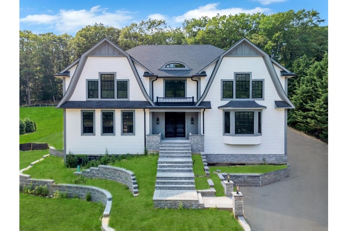 View of front facade featuring a gambrel roof, stairs, a front lawn, and a balcony