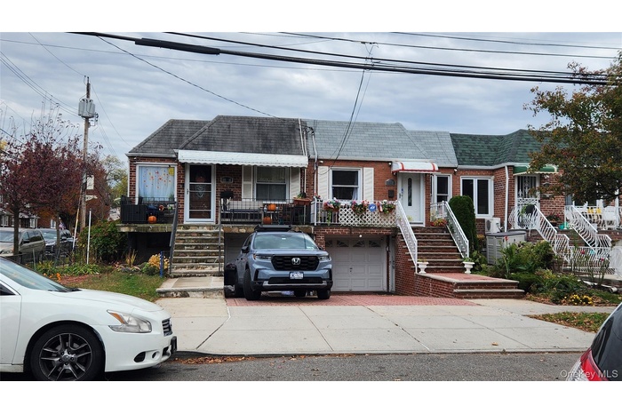 View of front facade featuring brick siding, stairway, roof with shingles, and concrete driveway