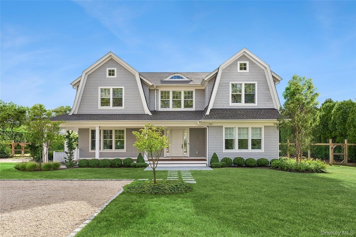 Shingle-style home featuring a gambrel roof, covered porch, a front lawn, and roof with shingles