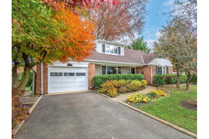 View of front facade featuring roof with shingles, asphalt driveway, brick siding, and an attached garage
