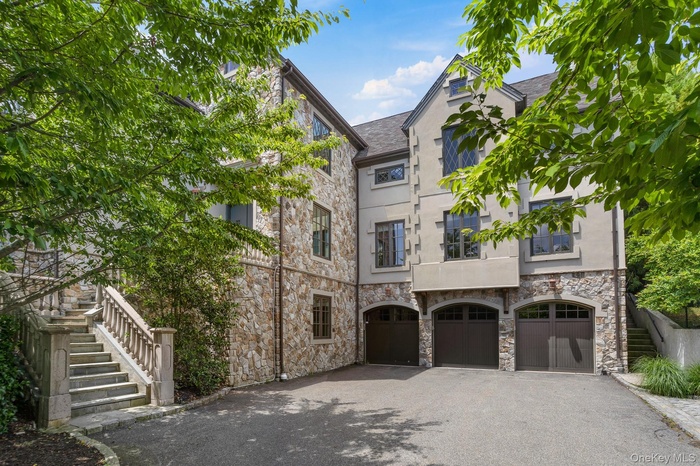 View of front facade with a garage, stairs, driveway, and stone siding