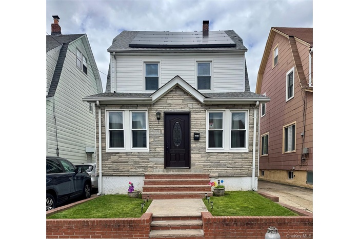 View of front of home featuring entry steps, stone siding, roof mounted solar panels, and a chimney