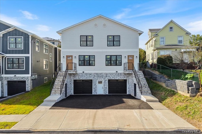 View of front of home with stairway, driveway, an attached garage, and stone siding