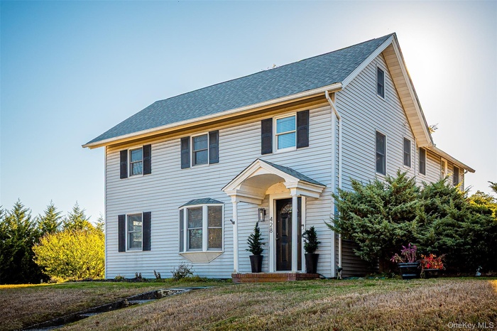 Colonial house featuring a shingled roof and a front lawn