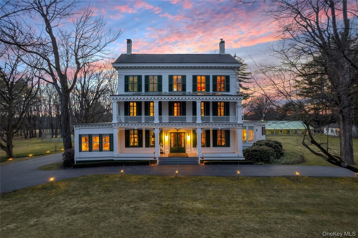 Back of property at dusk featuring a chimney, covered porch, and a yard