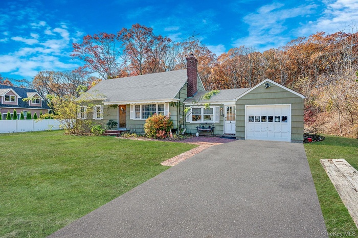 View of front facade featuring a chimney, asphalt driveway, a shingled roof, an attached garage, and a porch