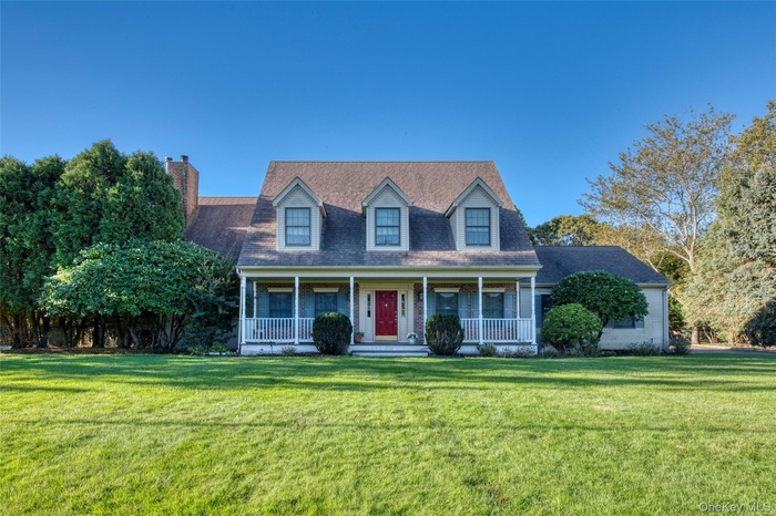 Cape cod home featuring covered porch, a front yard, roof with shingles, and a chimney